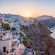 Traditional Greek buildings cascading down the cliffside with sailboats in the water below